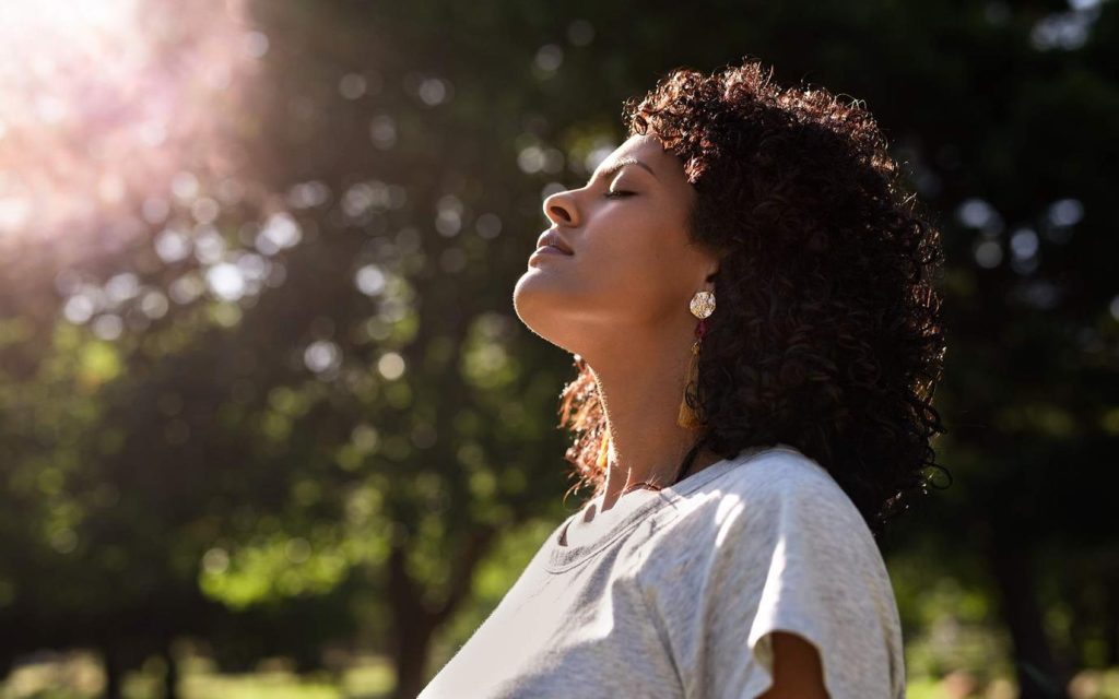 A woman with closed eyes tilts her face toward the sun