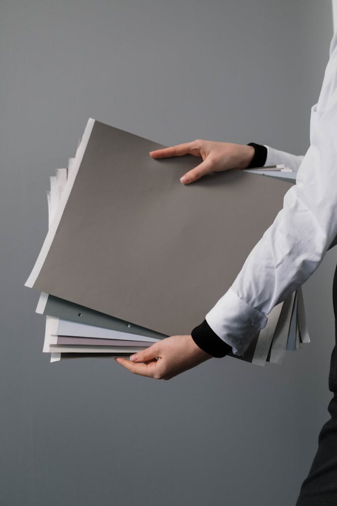 Close-up of hands holding a stack of colored and white papers in an office setting.