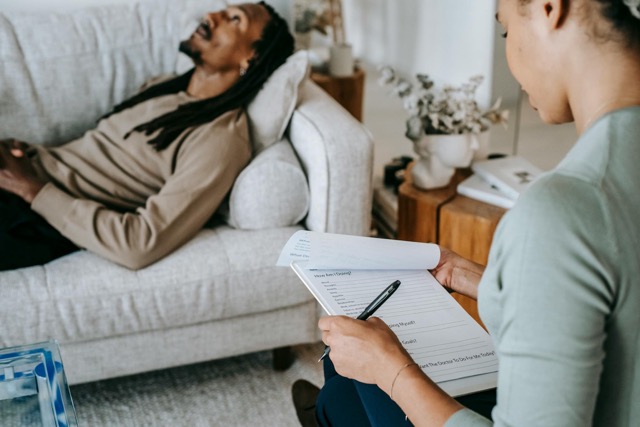 a-therapist-with-clipboard-assists-a-man-during-a-home-therapy-session